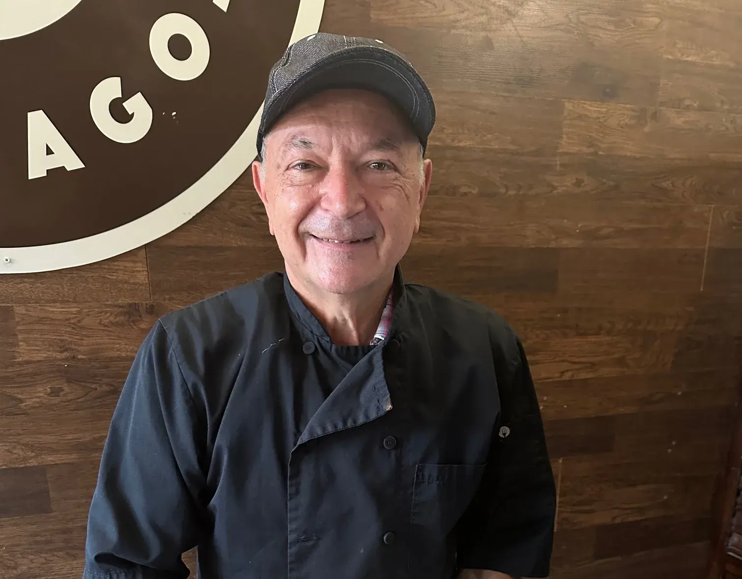 Chef Tony Barbanente smiling under the Anto Pizza Chicago logo on the dining room's wood wall