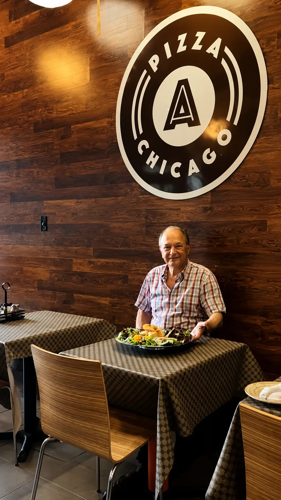 A guest smiling at his table with a plate of salad under the Anto Pizza Chicago logo