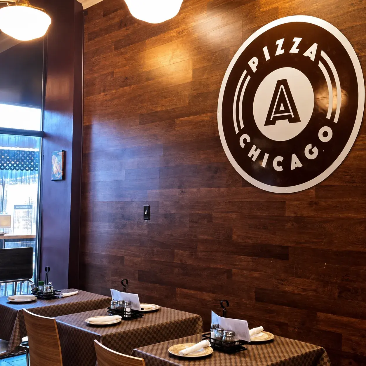 The Anto Pizza Chicago logo painted large on the dining room's wood wall above set tables
